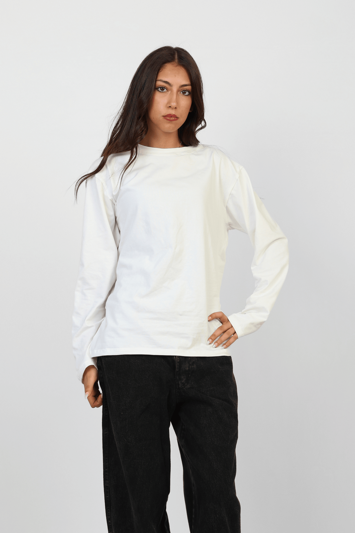 Woman wearing a white long-sleeve shirt and black pants on a light gray background